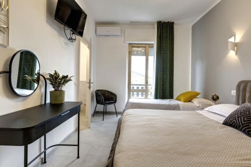 Modern hotel room at Palazzo Belvedere featuring two beds, balcony with landmark views, desk, and green accents