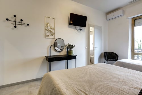 Modern hotel bedroom at Palazzo Belvedere with twin beds, black desk, round mirror, wall art, flat-screen TV, and balcony