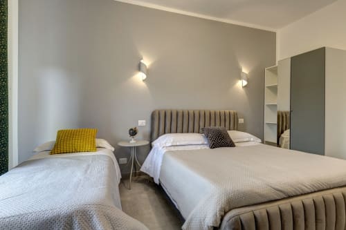Modern hotel room at Palazzo Belvedere with twin beds, taupe headboards, yellow pillow, and contemporary lighting in