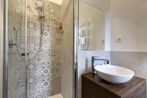 Modern bathroom at Palazzo Belvedere with decorative patterned tile shower, white vessel sink, and wood vanity in Chianciano