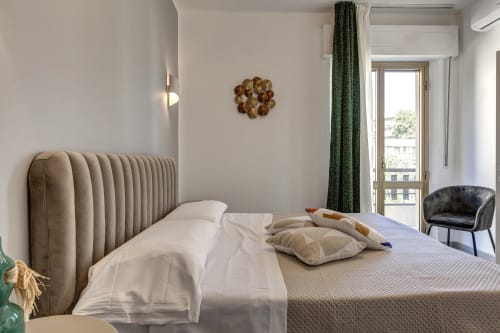Modern hotel bedroom at Palazzo Belvedere with beige upholstered bed, green curtains, balcony view, and contemporary