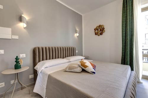 Modern bedroom at Palazzo Belvedere with taupe headboard, white bedding, green curtains, and balcony at Chianciano Terme