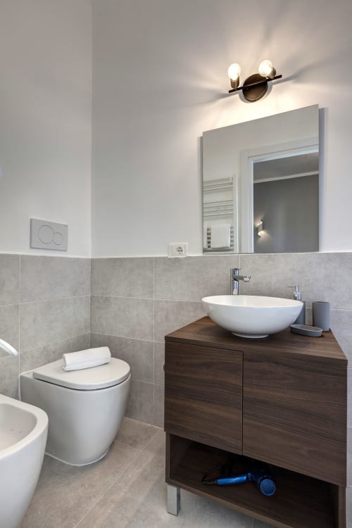 Modern bathroom at Palazzo Belvedere with white vessel sink, wooden vanity, toilet, and illuminated mirror