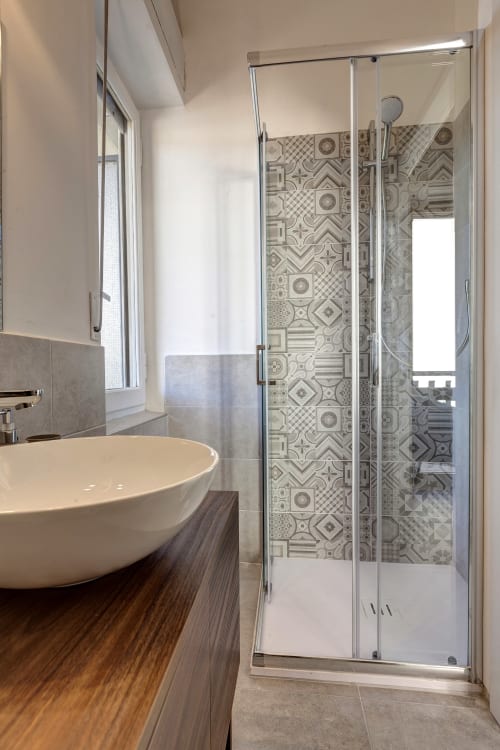 Modern bathroom at Palazzo Belvedere with round sink, patterned tile shower enclosure, and natural light from window