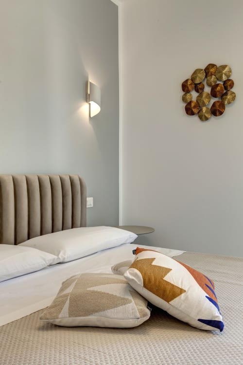 Modern bedroom at Palazzo Belvedere with beige upholstered headboard, decorative pillows, wall sconce lighting, and golden