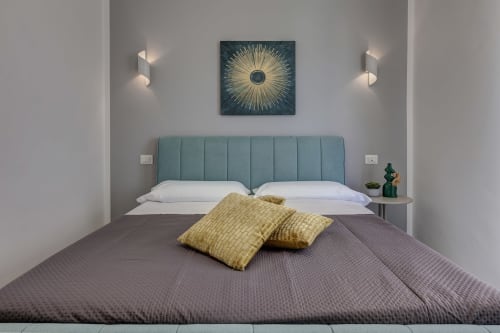 Modern bedroom at Palazzo Belvedere in Chianciano Terme with turquoise headboard, white pillows, and gold cushions