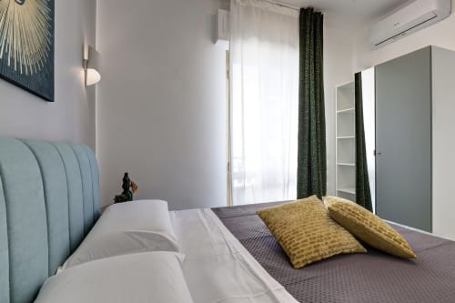 Modern bedroom at Palazzo Belvedere with blue upholstered headboard, yellow pillows, and floor-to-ceiling green curtains in