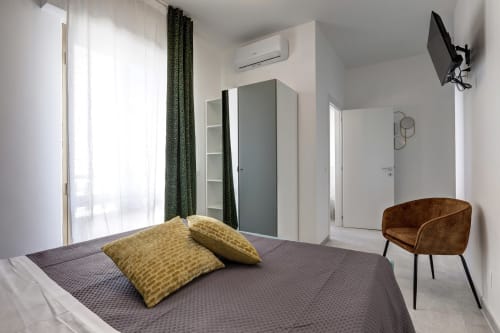 Modern bedroom at Palazzo Belvedere with queen bed, yellow pillows, brown chair, wardrobe, and balcony access in Chianciano