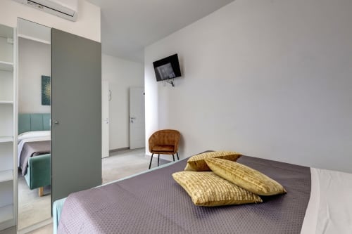 Modern hotel room at Palazzo Belvedere with bed, yellow pillows, armchair, and ensuite bathroom visible through open door