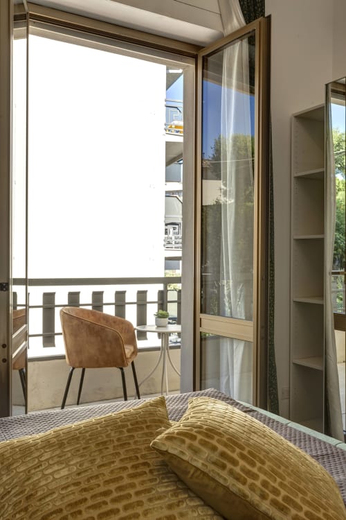 Bedroom with balcony view at Palazzo Belvedere in Chianciano Terme, featuring bed with yellow bedding, brown chair, and glass