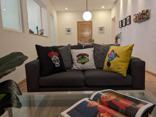 Sala moderna de Casa Donceles en Ciudad de México con sofá negro, cojines decorativos y arte colorido en paredes crema.