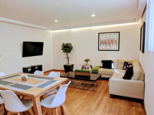 Área de estar moderna en Casa Donceles, Ciudad de México con sofá crema, mesa de comedor, televisor y plantas naturales