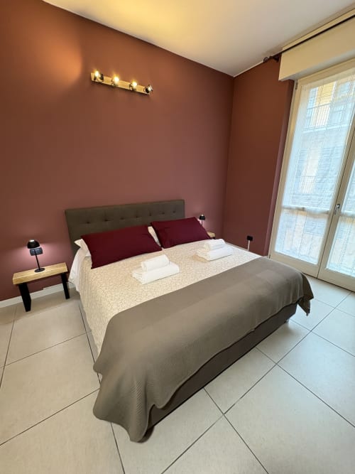 Camera moderna all'hotel Le Arche di Verona con pareti bordeaux, letto imbottito grigio, asciugamani bianchi e porte-finestre in vetro