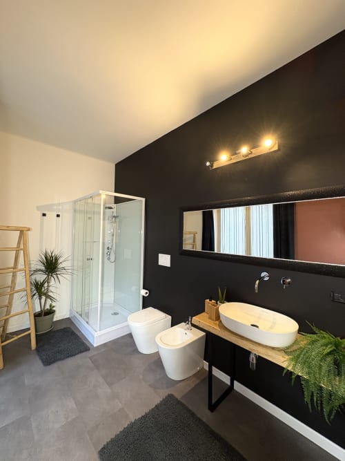 Bagno moderno dell'hotel Le Arche a Verona con parete nera, doppi lavabi vessel, doccia in vetro e design contemporaneo