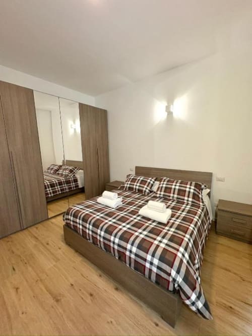 Camera da letto moderna a Le Arche, Verona con letto matrimoniale, biancheria a quadri, pavimento in legno e armadio con specchio