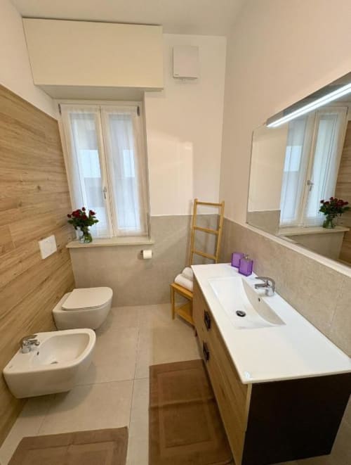 Bagno moderno dell'appartamento Le Arche a Verona con doppio lavabo, WC, bidet e accenti in legno