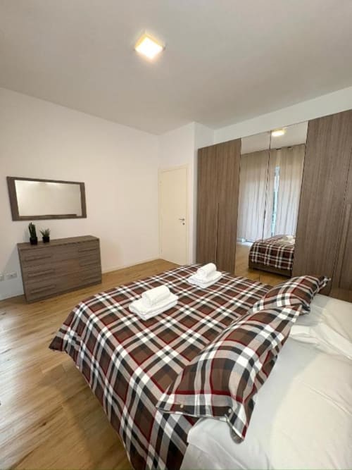 Ampia camera da letto in appartamento Dimora Vittoria presso l'hotel Le Arche a Verona, con letto coperto da coperta scozzese e pavimenti in legno