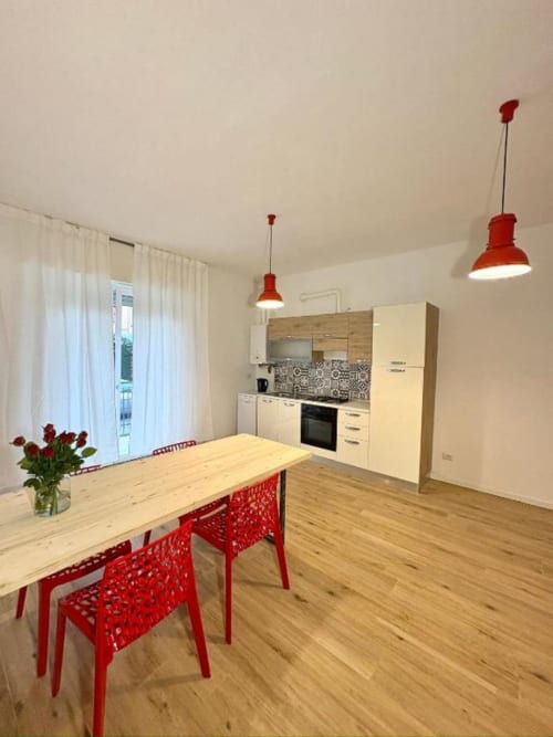 Moderna cucina e zona pranzo dell'appartamento Le Arche a Verona con accenti rossi e tavolo in legno