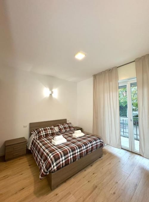 Camera luminosa in appartamento Dimora Vittoria a Verona con biancheria a quadri, pavimento in legno e porte vetrate sul balcone