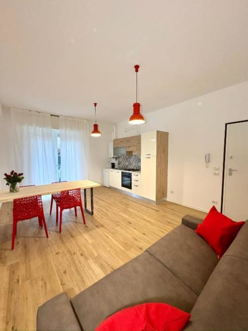 Moderno soggiorno e cucina dell'hotel Le Arche a Verona con accenti rossi, zona pranzo e pavimenti in legno