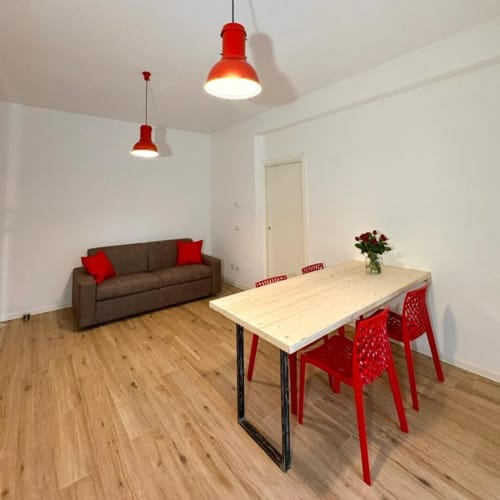 Zona pranzo moderna di Le Arche Verona con lampade a sospensione rosse, tavolo in legno e divano marrone