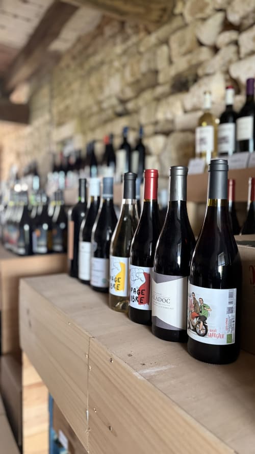 Wine bottles displayed on wooden table at La Guirtelle B&B in Lainsecq, France, with stone cellar backdrop