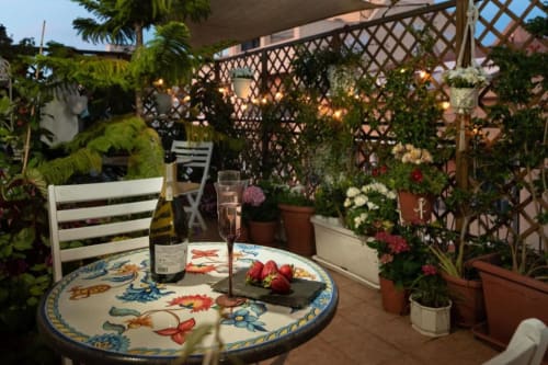 Terrazza del B&B Roof Garden di Alghero al tramonto con tavolo decorativo, bottiglia di vino, piante fiorite e pergolato in legno