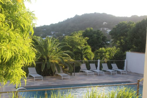 Espace solarium avec transats blancs au bord de la piscine, vue dégagée sur les mornes - Location vacances familles.