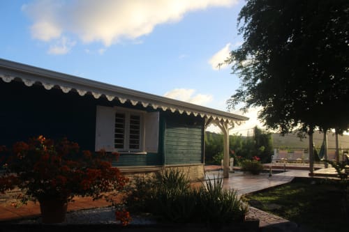 Façade de villa créole traditionnelle en bois bleu avec lambrequins et jardin fleuri au coucher du soleil - Location Sud Martinique