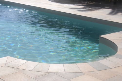 Gros plan sur l'eau cristalline et scintillante de la piscine avec dallage beige soigné - Entretien impeccable Villa Caryota.