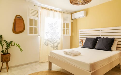 Chambre double lumineuse aux murs jaunes avec décoration tropicale soignée et climatisation - Location Villa Martinique.