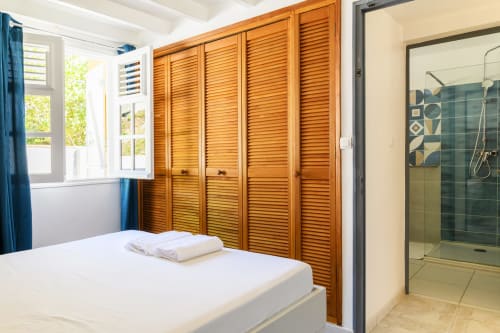 Suite confortable avec dressing en bois, rideaux bleus et vue sur la salle de douche moderne attenante - Villa Le Marin.