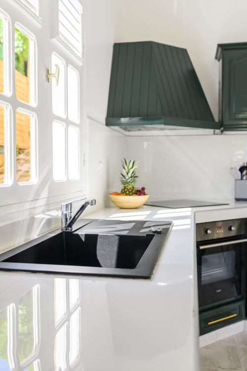 Cuisine moderne entièrement équipée avec placards vert émeraude, plan de travail blanc et fenêtre lumineuse - Villa Caryota.