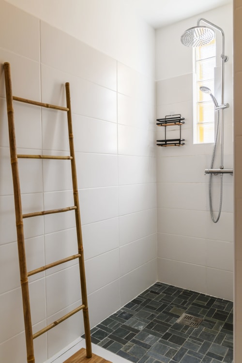 Salle de douche moderne et lumineuse avec colonne de pluie, sol en pierre grise et échelle en bambou zen - Villa Caryota.