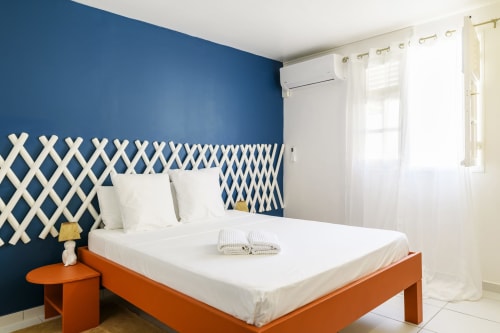 Chambre au design audacieux : mur bleu profond, tête de lit graphique blanche et mobilier orange vibrant - Villa Caryota.
