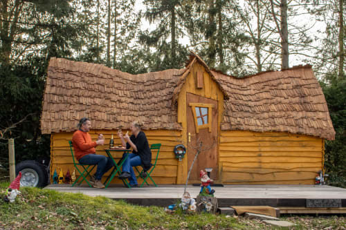 Paar genießt Getränke auf grünen Stühlen vor einem bezaubernden gelben Holzhaus mit Holzschindeldach bei Les Refuges Du