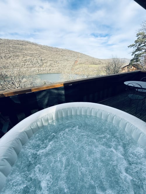 Vasca idromassaggio con acqua frizzante sulla terrazza del lodge che si affaccia sul lago e sulle montagne boscose delle Cabanes du Belvédère