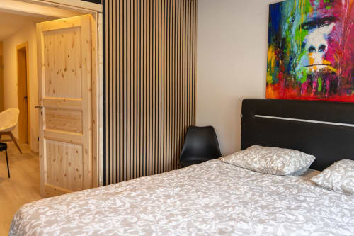 Chambre moderne aux Louettes B&B à Saxon avec lit queen-size, art abstrait coloré et porte en bois menant à la salle d'eau.