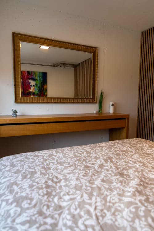 Chambre aux Louettes B&B à Saxon avec lit, bureau en bois, miroir et œuvres d'art colorées