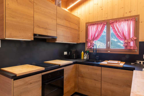 Cuisine alpine moderne avec meubles en bois, plan de travail noir et rideaux à carreaux rouges au Chalet d'hôtes Les Louettes, Saxon