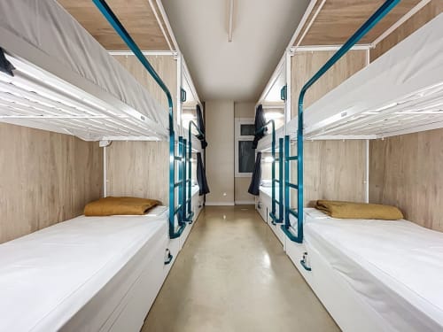 Female dorm room at Lemon Hostel Altea with bunk beds, blue metal frames, white bedding, wooden accents, and central aisle in