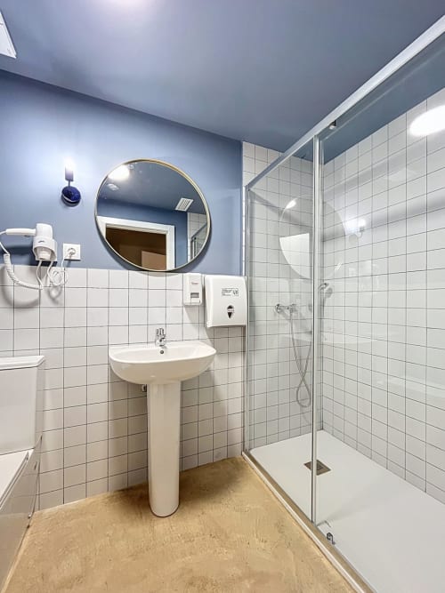 Modern bathroom at Lemon Hostel Altea with pedestal sink, round mirror, shower enclosure, and white tile walls