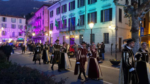 Evening street festival in Bellano, Italy with performers in medieval costumes and colorful illuminated buildings
