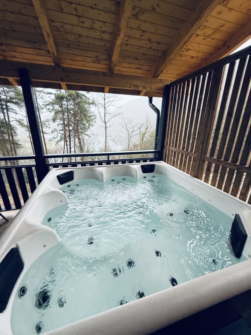 Heated outdoor hot tub with jets on a wooden deck overlooking mountain views at Cabanes et lodges du Belvédère