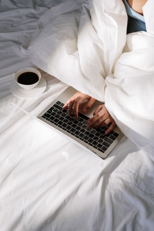 Ospite che lavora al laptop a letto presso l'hotel Centro Da Viola di eco design a Olba, Italia, con caffè
