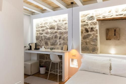 Camera d'hotel eco-design moderno a Olbia con muri in pietra, area di lavoro e biancheria bianca con vista su pietra a vista