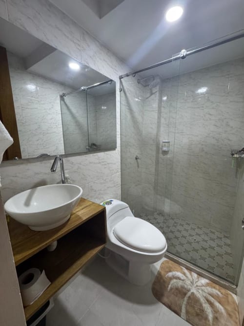 Baño moderno del hotel Olamar Living en Santiago de Tolú con pisos de mármol, lavamanos de recipiente, inodoro y ducha con encierro de cristal