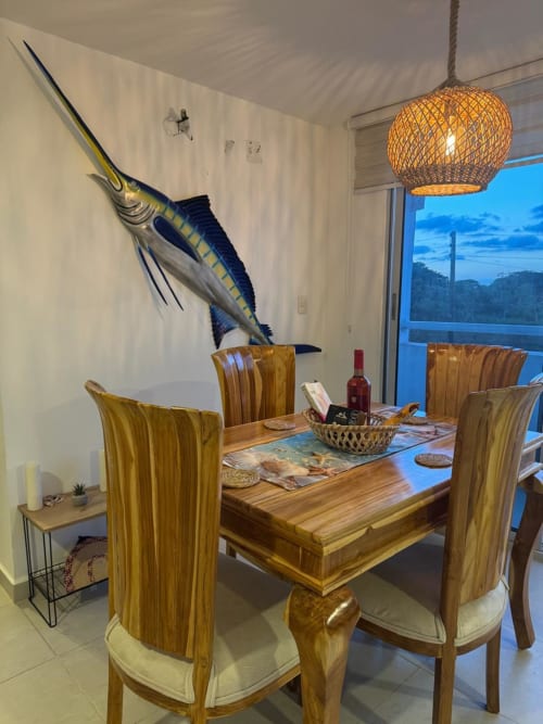 Comedor moderno en Olamar Living con mesa de madera, sillas rayadas, arte con marlin, lámpara colgante tejida y montaña