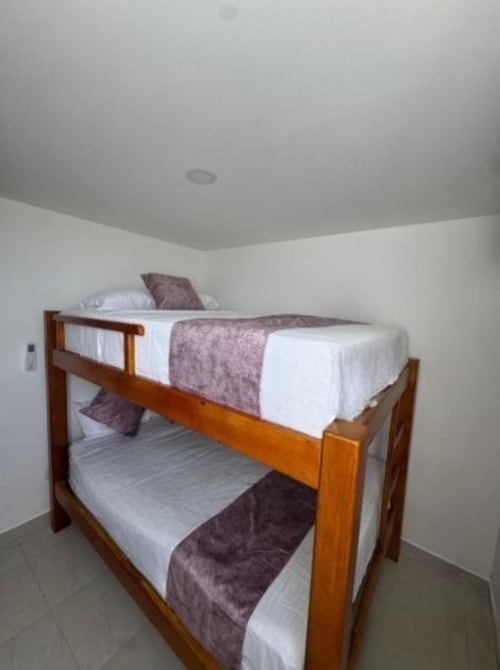 Litera con estructura de madera y sábanas blancas en apartamento Olamar Living, Coveñas, Colombia