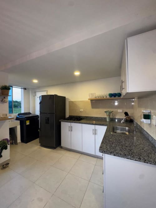Moderna cocina con encimeras de granito, armarios blancos, electrodomésticos negros, fregadero de acero inoxidable y vistas a la montaña en Olamar